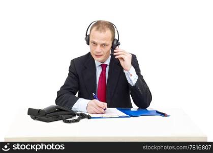 A businessman in a gray suit and tie behind a desk making a telephone call using a head set