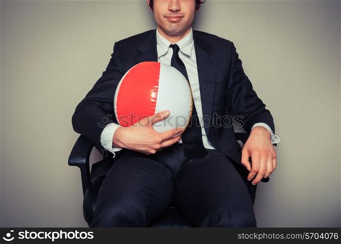 A businessman is sitting in an office chair with a beach ball