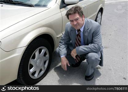 A businessman on the road with a flat tire. He looks upset.