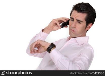 A businessman over the phone looking at his watch.