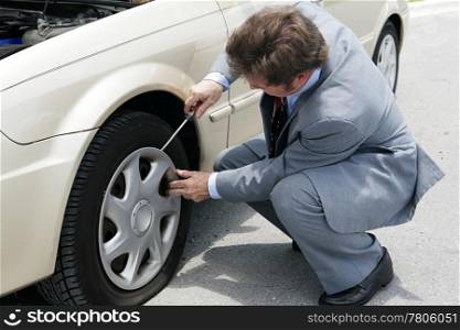 A businessman prying off the hubcap of his flat tire.