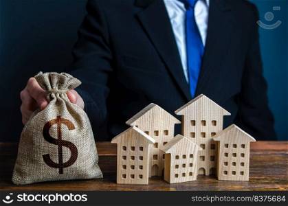 A businessman puts a dollar money bag near the houses. Investments in real estate assets. Construction industry, rental business and hotel tourism. Municipal budget of the city. Official.