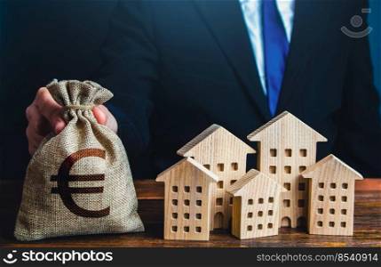 A businessman puts a euro money bag near the houses. Investments in real estate assets. Municipal budget of the city. Official. Construction industry, rental business and hotel tourism.