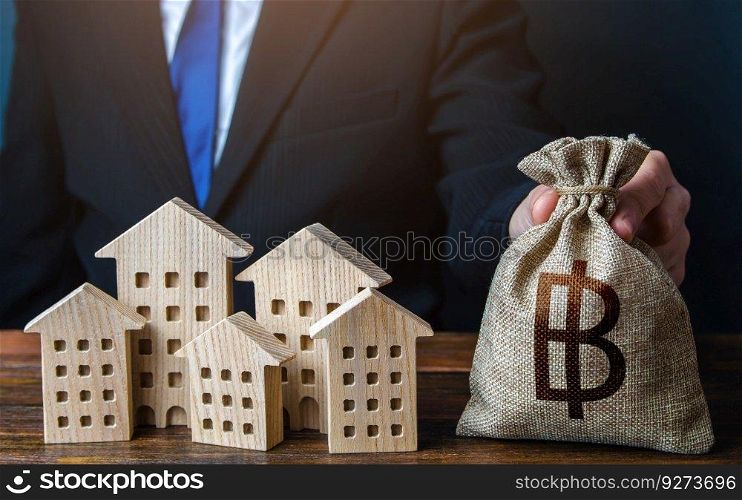 A businessman puts a thai baht money bag near the houses. Construction industry, rental business and hotel tourism. Investments in real estate assets. Municipal budget of the city.