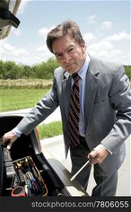 A businessman rooting in his trunk for tools to repair his broken down car.