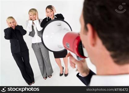 A businessman shouts through a megaphone while three business woman cover their ears and scream