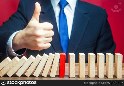A businessman shows a thumbs up approval over a stopped process falling domino. Find a way stop the problem and prevent its spread. Achieving success and completing a task. Solution. Cyber protection