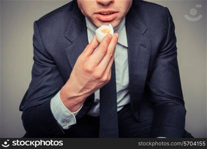 A businessman sitting in an office chair is eating an egg