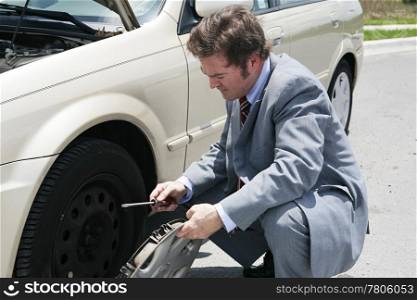 A businessman, stranded with a flat tire, removes his hubcap.