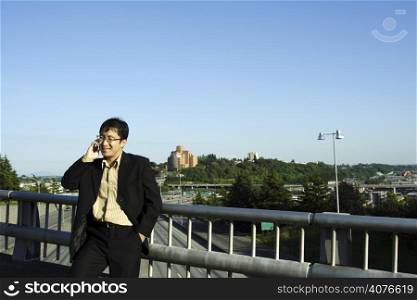 A businessman talking on the phone on a bridge over a highway