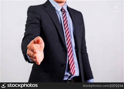A businessman wearing a suit extends his right hand to shake hands.
