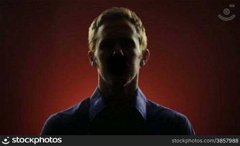 A businessman, whose face is hidden in shadow, stares into the camera in front of a red background. Off-centered version also available.