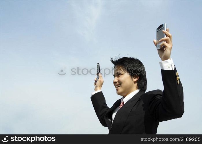 A businessman with arms up in the air holding a PDA and a cell phonee