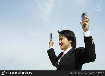 A businessman with arms up in the air holding a PDA and a cell phonee