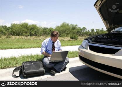 A businessman working in the sun by the side of his broken down car.