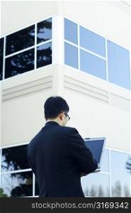 A businessman working on his laptop outside his office buildings