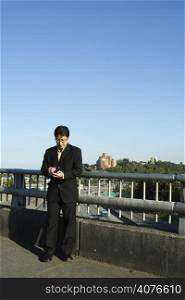 A businessman working on his PDA on a bridge