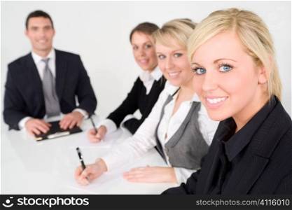 A businesswoman and a team of 2 women and a man out of focus behind her having a meeting