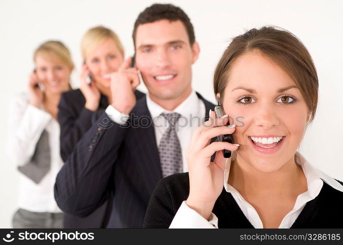 A businesswoman and three colleagues out of focus behind her all talking on cell phones