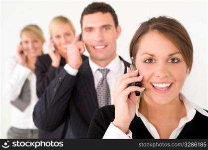 A businesswoman and three colleagues out of focus behind her all talking on cell phones