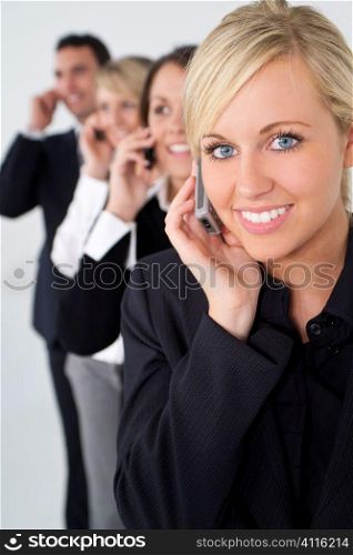 A businesswoman and three colleagues out of focus behind her all talking on cell phones