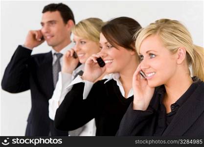 A businesswoman and three of her colleagues out of focus behind her all talking on cell phones