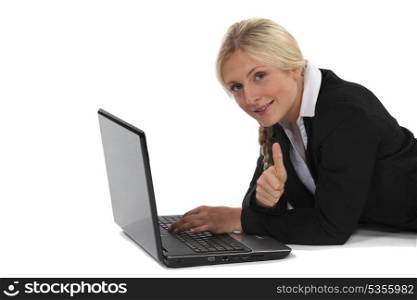 A businesswoman lying on the floor with her laptop.