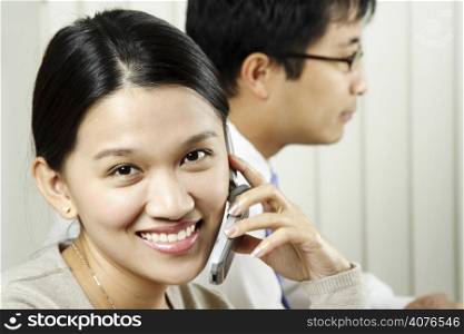 A businesswoman making a phone call with a businessman in the background