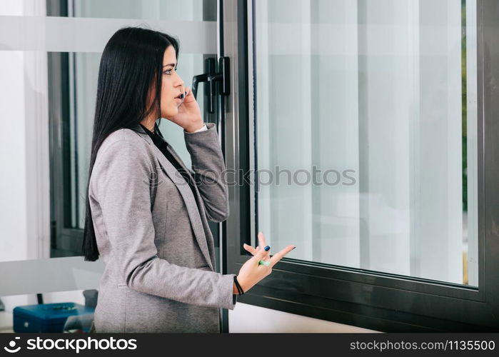 A businesswoman talking by cellphone near a window in the office