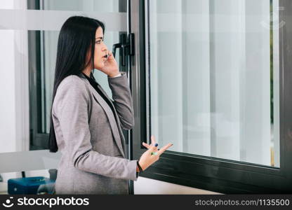 A businesswoman talking by cellphone near a window in the office