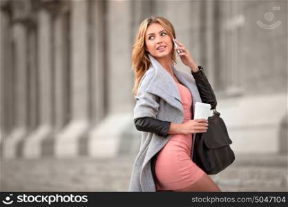 A businesswoman talking via mobile phone and holding a coffee cup against urban scene.