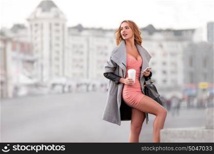 A businesswoman with a mobile phone holding a coffee cup against urban scene.
