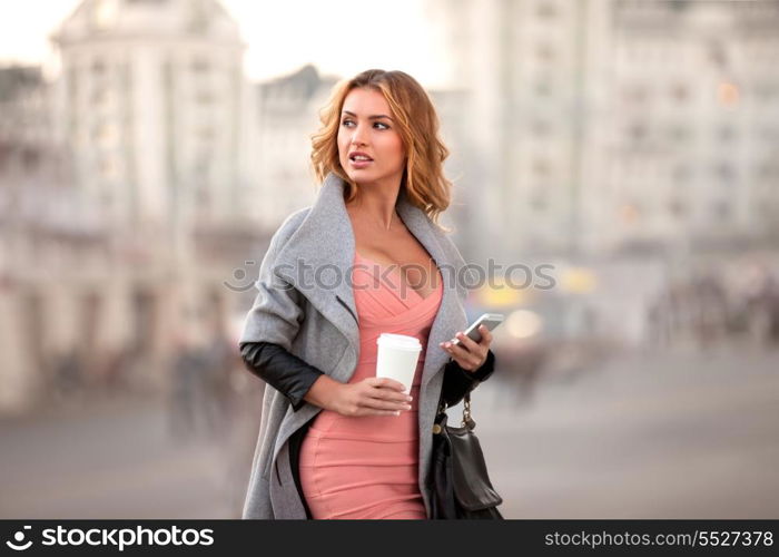 A businesswoman with a mobile phone holding a coffee cup against urban scene.