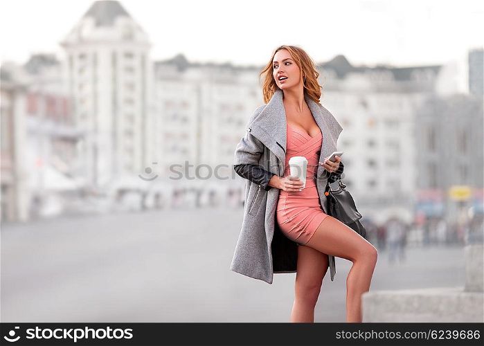 A businesswoman with a mobile phone holding a coffee cup against urban scene.