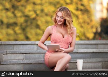 A businesswoman with a tablet and coffee cup sitting on stairs.