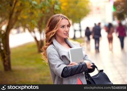 A businesswoman with a tablet walking in a city park.