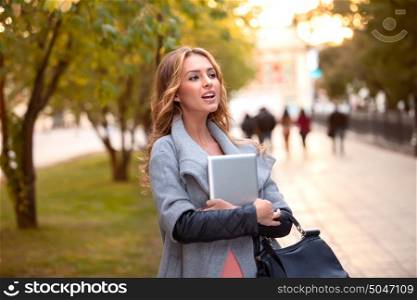 A businesswoman with a tablet walking in a city park.
