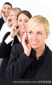 A businesswoman with three other executives out of focus behind her all talking on cell phones