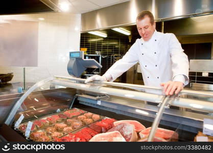 A butcher at a fresh meat counter in a grocery store