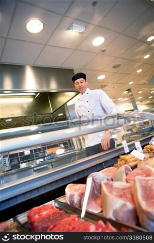 A butcher looking at a fresh meat counter in a grocery store