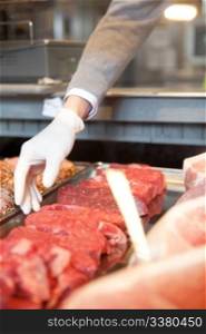 A butcher&rsquo;s hand reaching into a cooler picking a fresh cut of meat