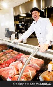 A butcher standing behind a fresh meat counter smiling at the camera