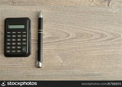 A calculator and pen displayed on a wooden background