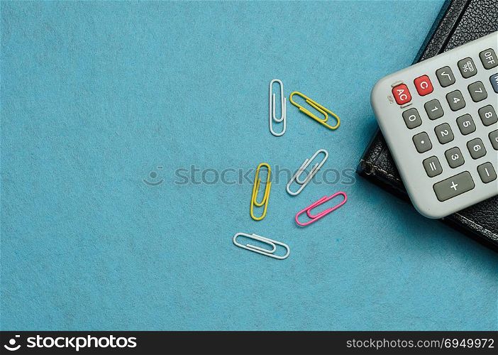 A calculator, paperclips and a book displayed on a blue background