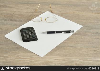 A calculator, pen, reading glasses and a piece of paper displayed on a wooden background