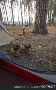 a camping aesthetics. view from the tent on hiking boots and a burner with a boiler on the background of the forest