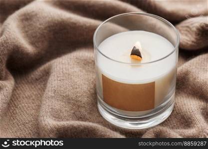 A candle burns on the background of a knitted sweater. The concept of cozy winter or autumn.