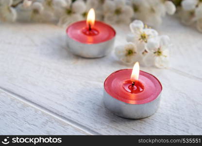 A candle stands on a wooden white table near the branches of white flowers of cherry. close-up.. A candle stands on a wooden white table near the branches of white flowers of cherry.