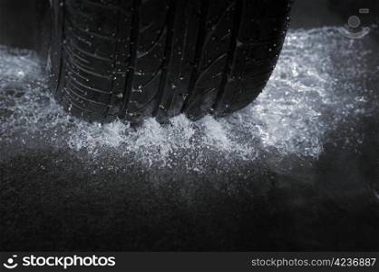 A Car tire on a wet road. The rain groove is a design element of the tread pattern specifically arranged to channel water away from the footprint.