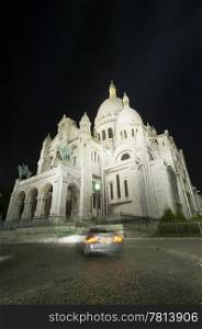 A car turning in front of the SacrZ Coeur at night, using a wide angle perspective. The illumination of the church makes it stand out beautifully against the dark sky.